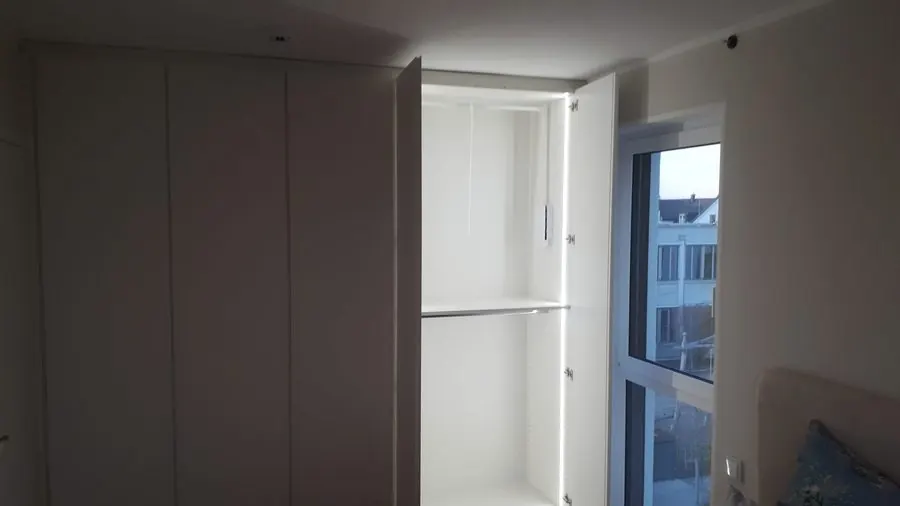 Raumhoher weißer Einbauschrank im Schlafzimmer, eine Tür offen, LED im Innenraum — Björn Schillinger Schreinermeister, Germering